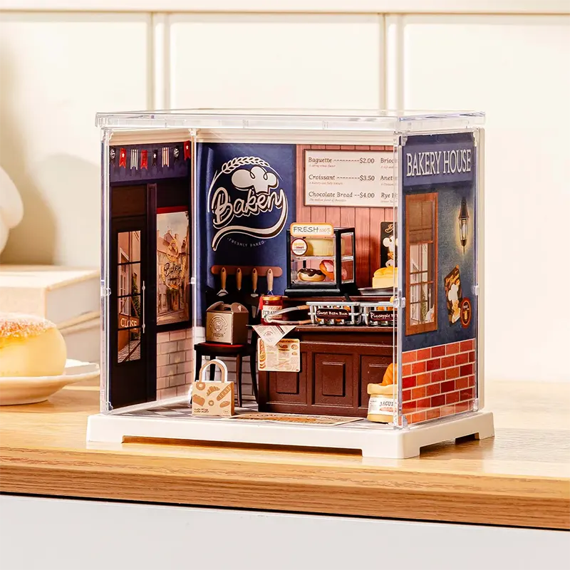 Miniature bakery model in a clear display case on a wooden surface.