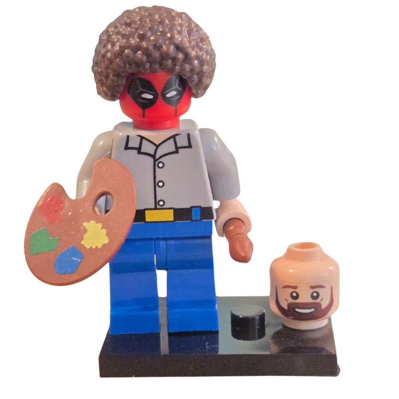 A custom Lego minifigure resembling a character painting a picture, with a predominantly red and yellow hairstyle, wearing a gray shirt and blue pants, holding a paintbrush, alongside a small, stylized version of a human head.