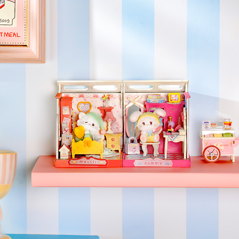 A miniature dollhouse playset with two rabbit characters in colorful rooms, displayed on a pink shelf against a blue and white striped wall.
